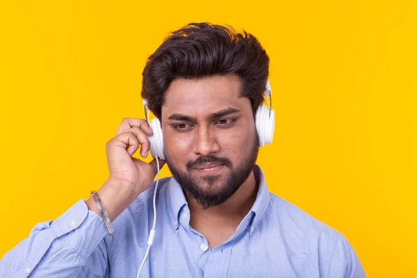 Bel homme indien détendu avec barbe écoute de la musique préférée aux écouteurs sur fond jaune. Concept d'abonnement musical et radio en ligne . — Photo