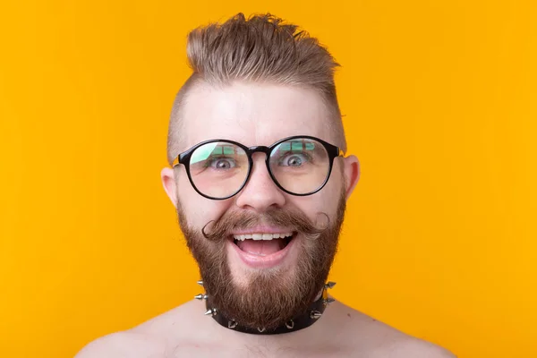 Joven hombre de moda positivo hipster con una barba bigote y collar fetiche en camisa posando sobre un fondo amarillo. Concepto de roca y subcultura . — Foto de Stock