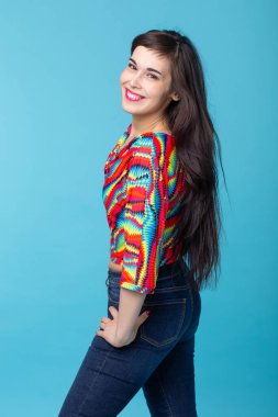 Uzun saçlı neşeli genç esmer kadın mavi bir arka planda poz. Güzel ve bakımlı bir kadın kavramı