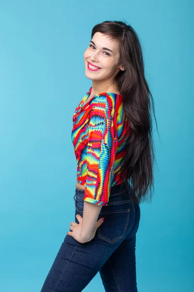 Jovem morena alegre com cabelos longos posando em um fundo azul. O conceito de uma mulher bonita e bem tratada — Fotografia de Stock