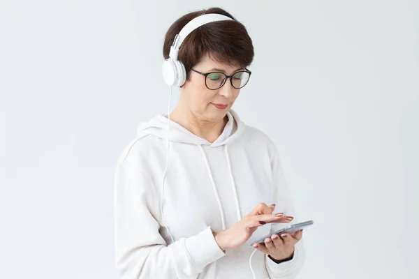 Beautiful woman 40-50 years old listening music in big headphone holding tablet on white background — Stock Photo, Image