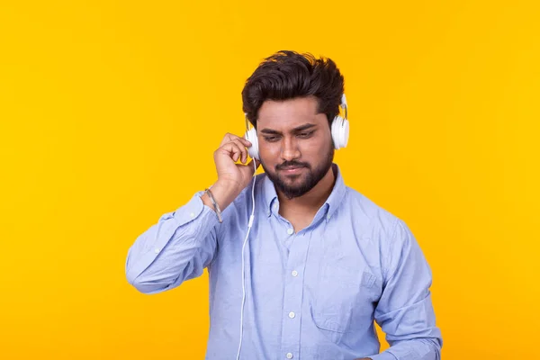 Portrait of a positive young indian man with a beard listening to an audiobook on yellow background. Leisure learning concept. — Stock Photo, Image