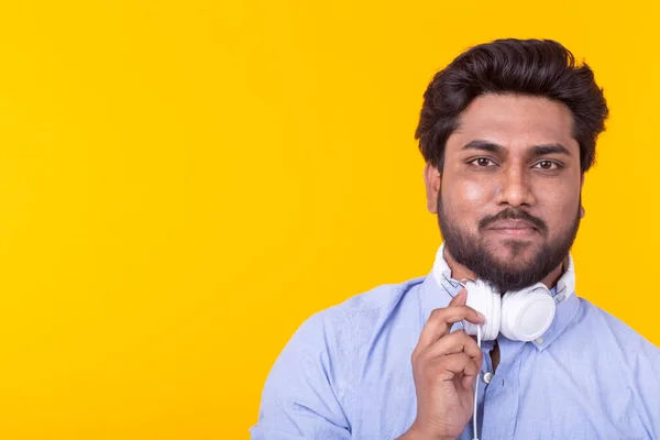 Pozitív fiatal indiai férfi hallgat a kedvenc online rádió segítségével okostelefon fejhallgató és nagy sebességű vezeték nélküli internet a sárga háttér másolási tér — Stock Fotó