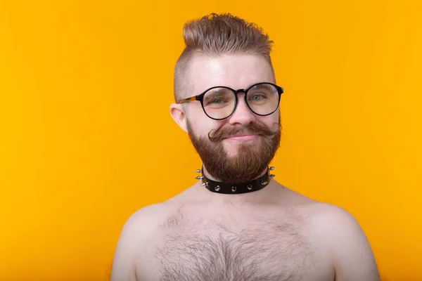 Joven hombre de moda positivo hipster con una barba bigote y collar fetiche en camisa posando sobre un fondo amarillo. Concepto de roca y subcultura . —  Fotos de Stock