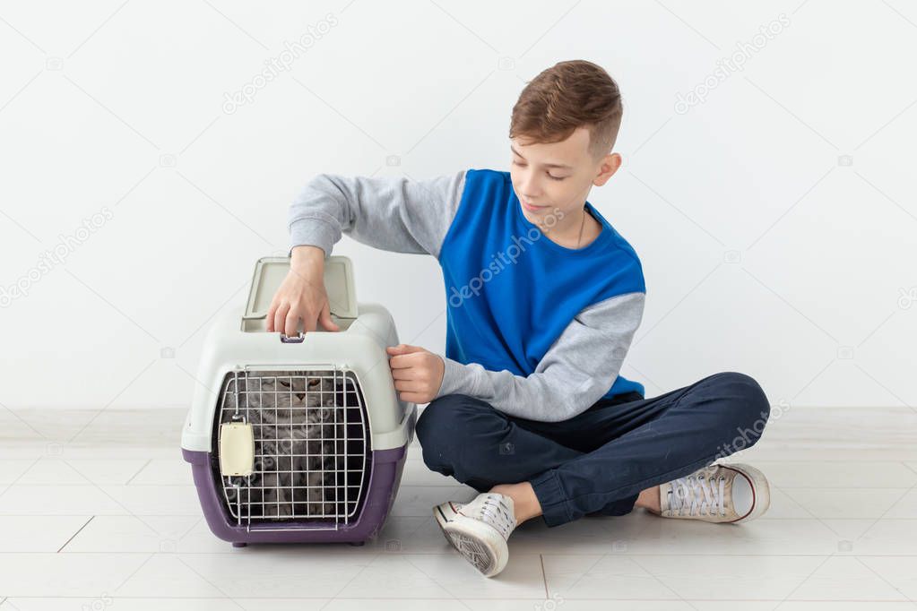 Laughing little positive boy holds a cage with a scottish fold cat next to him sitting on the floor in a new apartment. Pet protection concept.