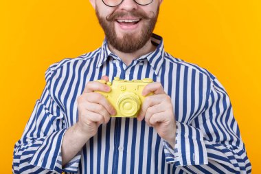 Bıyığı ve sarı arka planda sakal olan sarı kamera olan tanımlanamayan genç adam. Konsept fotoğrafçılığı ve hobi.