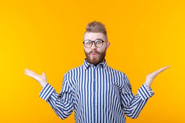 Bıyık ve sakallı genç adam sarı bir arka planda sürpriz gözleri şişkinleme yapıyor. Sürpriz ve belirsizlik kavramı.