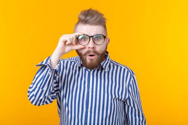 Bıyık ve sakallı genç adam sarı bir arka planda sürpriz gözleri şişkinleme yapıyor. Sürpriz ve belirsizlik kavramı.