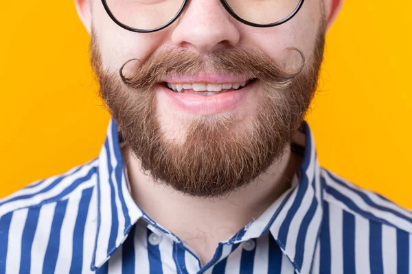 Un joven no identificado con bigote y barba sonriendo sobre un fondo amarillo . — Foto de Stock