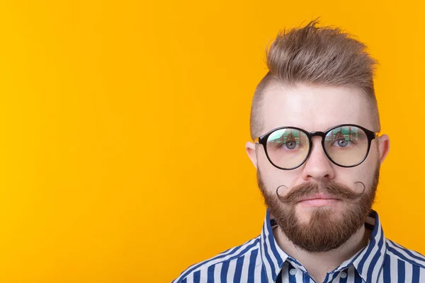 Young positive trendy man hipster with a mustache beard and fetish necklace in shirt posing on a yellow background with copy space. Concept of rock and subculture. — Stock Photo, Image