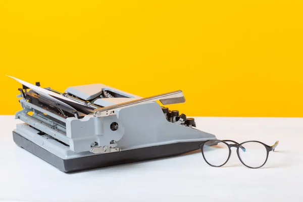 Lugar de trabajo del gerente de la secretaria y la máquina de escribir de negocios y gafas están sobre la mesa sobre un fondo amarillo. Concepto de trabajo . — Foto de Stock