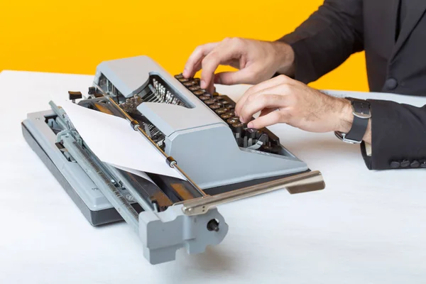 Primer plano del empresario o gerente en traje formal escribiendo texto en una máquina de escribir sobre un fondo amarillo. Concepto de trabajo empresarial y de oficina — Foto de Stock