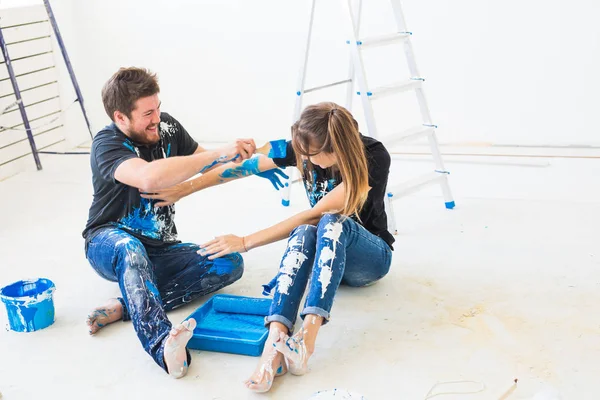 Renovation, redecoration and interiors concept - Young couple sitting on the white floor and pour paint and having fun — Stock Photo, Image