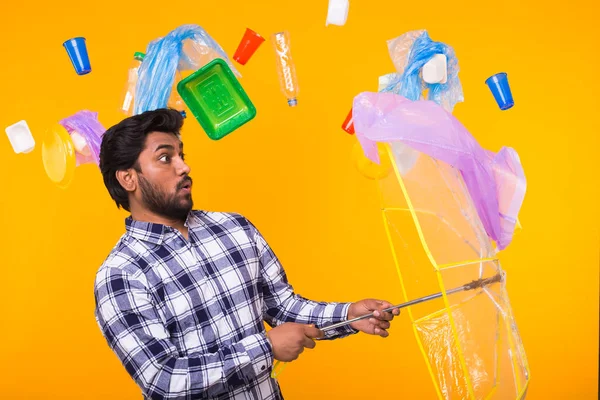 World Environment Day, plastic recycling problem and environmental disaster concept - Surprised Indian man trying to hide from garbage under an umbrella on yellow background — Stock Photo, Image