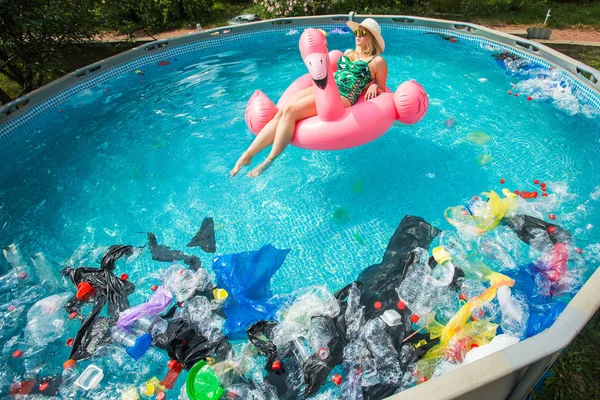 Problema de lixo, reciclagem de plástico, poluição e conceito ambiental - mulher boba nada e se divertir em uma piscina poluída. Garrafas e sacos de plástico flutuam perto dela — Fotografia de Stock