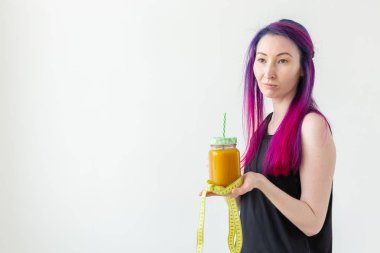 Tanımlanamayan genç kız hipster bir saman ile meyveli protein suyu tutan ve kopya alanı ile beyaz arka plan üzerinde bant ölçme. Sağlıklı beslenme ve iyi fitness anlayışı.