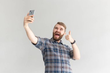 Olumlu bir komik yakışıklı hipster adam yan görünümü ve beyaz arka plan üzerinde bir akıllı telefon selfie alarak. Gadget'lar ve modern teknolojiler kavramı.