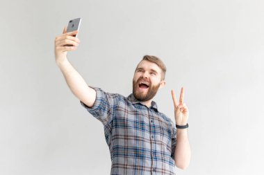 Olumlu bir komik yakışıklı hipster adam yan görünümü ve beyaz arka plan üzerinde bir akıllı telefon selfie alarak. Gadget'lar ve modern teknolojiler kavramı.