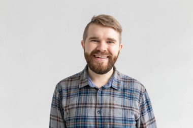 Gülümseyen sakallı genç adam, beyaz arka plan üzerinde, rahat giyinmiş, hafta sonları geliyor sevinir. Pozitif memnun öğrenci.