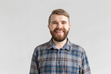 Gülümseyen sakallı genç adam, beyaz arka plan üzerinde, rahat giyinmiş, hafta sonları geliyor sevinir. Pozitif memnun öğrenci.