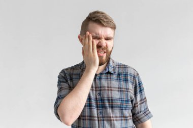 Diş ağrısı kavramı. Genç erkek kapalı çekim ağrı hissi, el ile yanağını tutarak, beyaz arka plan üzerinde kötü diş ağrısı muzdarip