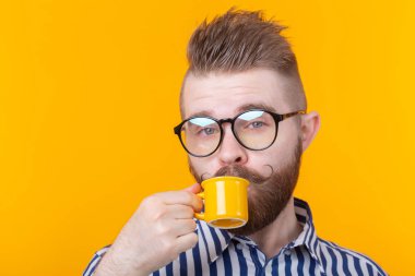 Sevimli kendine güvenen genç adam sarı bir arka plan karşısında dururken küçük bir sarı kupa kahve içme. Sabah kahvesi veya espresso konsepti.
