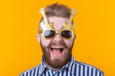 Gitar şeklinde gözlüklü pozitif genç adam sarı bir arka plan karşı sevinir. Kutlama ve partiler kavramı.