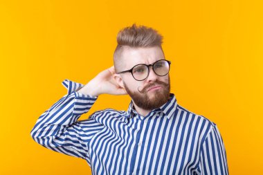 Gözlüklü ve sarı arka planda poz veren sakallı şık bir saç modeline sahip pozitif bir genç erkek öğrencinin portresi. Erkekler için Berber dükkanı konsepti ve güzellik salonu.
