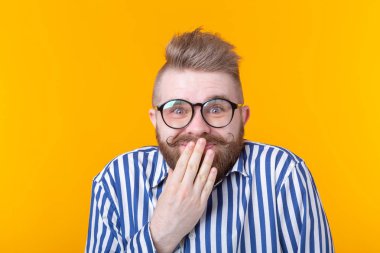 Gözlüklü şaşıran genç erkek hipster ağzını kapatır ve sarı bir arka plan üzerinde poz güler. Çizim ve sürpriz kavramı.