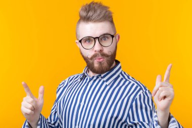 Bıyıklı ve sakallı pozitif genç adam mutlu bir şekilde parmağını yukarı doğru işaret ediyor ve sarı bir arka plan üzerinde yararlı bir şey gösteriyor. Önemli bilgi kavramı.