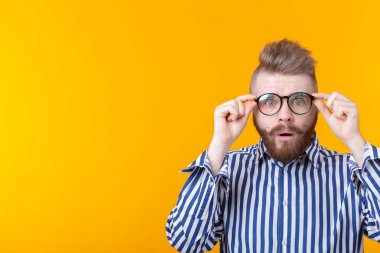 Bıyıklı ve sakallı genç hipster adam kopya alanı ile sarı bir arka plan üzerinde poz gözlük ile bakar. Sürpriz kavramı.