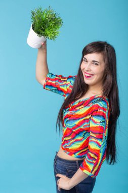 Neşeli genç kadın mavi bir arka plan karşı poz bir bitki ile bir pot tutuyor. Bahçe ve iç aksesuar konsepti.