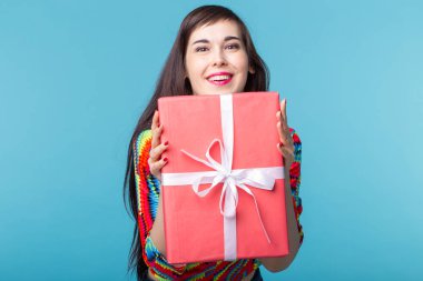 Mavi bir arka planda ayakta iken elleri kırmızı hediye kutusu tutan ince güzel genç esmer kız. Pay ve ikramiye konsepti.