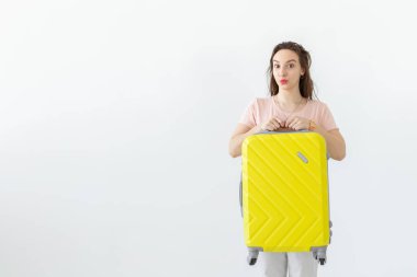 Fotokopi alanı ile beyaz arka plan üzerinde bir tatil beklerken sarı bir bavul ile poz neşeli gülümseyen genç esmer kadın. Turizm ve seyahat kavramı