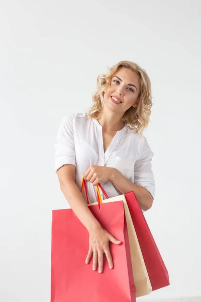 Pozitív, fiatal, stílusos szőke nő, aki olyan táskák pózol fehér alapon. Shopping koncepció egy bevásárlóközpontban. — Stock Fotó