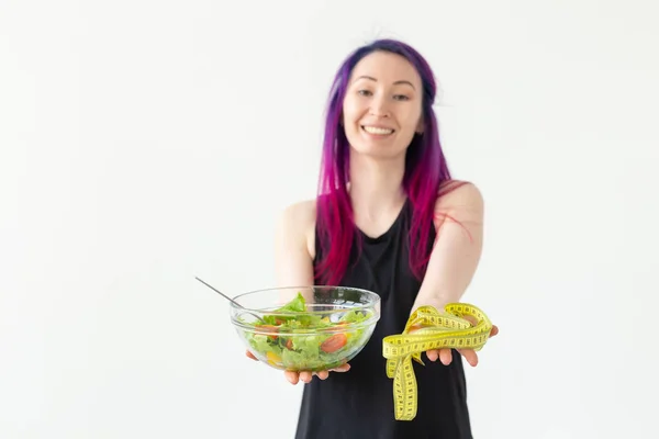 Тонка молода азіатська дівчина з кольоровим волоссям тримає вимірювальну стрічку і тримає в руках легкий овочевий салат, позує на білому тлі. Здорове харчування концепції. Копіспазмі . — стокове фото