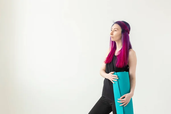 Junges nettes Mädchen Hipster mit farbigen Haaren hält in der Hand eine Sportmatte posiert auf einem weißen Hintergrund mit Kopierraum. Konzept eines gesunden Lebensstils. — Stockfoto