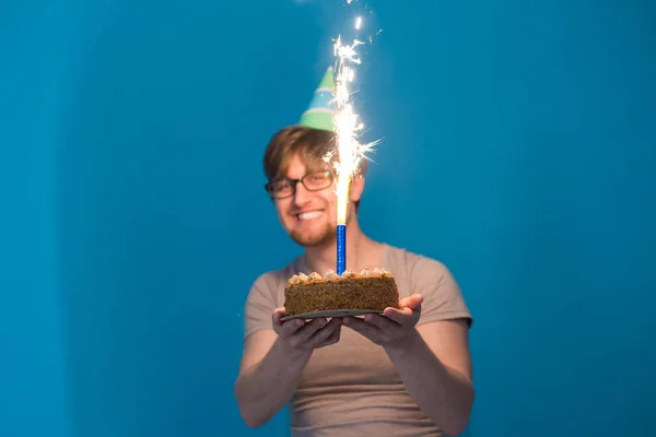 Gözlüklü çılgın neşeli adam öğrenci elinde havai fişek yanan bir pasta tutan bir kağıt şapka ile tebrik. Tatil Doğum günü konsepti — Stok fotoğraf