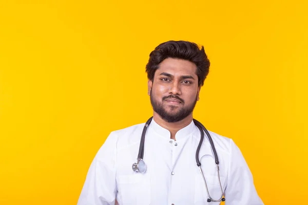 Jeune médecin indien positif en manteau blanc avec un stéthoscope posé sur un fond jaune. Concept de médecine efficace et conseils des médecins . — Photo