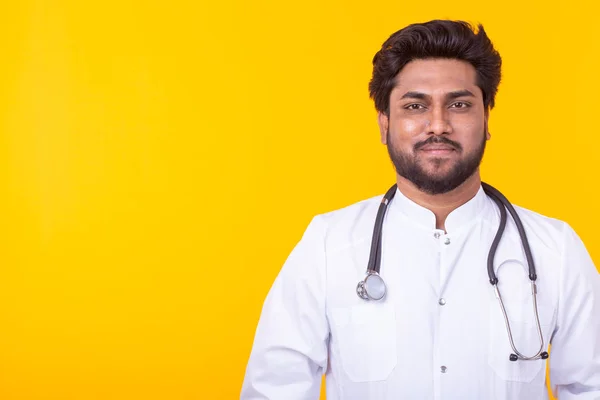 복사 공간이있는 노란색 배경에 포즈를 취한 청진기를 가진 흰색 코트를 입은 긍정적 인 젊은 인도 의사. 효과적인 의학 및 의사 조언의 개념. — 스톡 사진