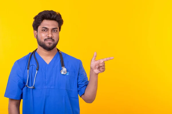 Médico indio varón con un estetoscopio posando sobre un fondo amarillo apuntando al espacio de copia. Concepto de tratamiento y recuperación . —  Fotos de Stock