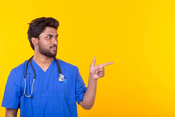 청진기를 가진 남성 인도 의사가 카피 스페이스를 가리키는 노란색 배경에 포즈를 취하고 있습니다. 치료 및 회복의 개념. — 스톡 사진