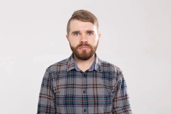 Jonge man met een snor en baard maken uitpuilende ogen in verrassing tegen een witte achtergrond. Concept van verrassing en onzekerheid. — Stockfoto