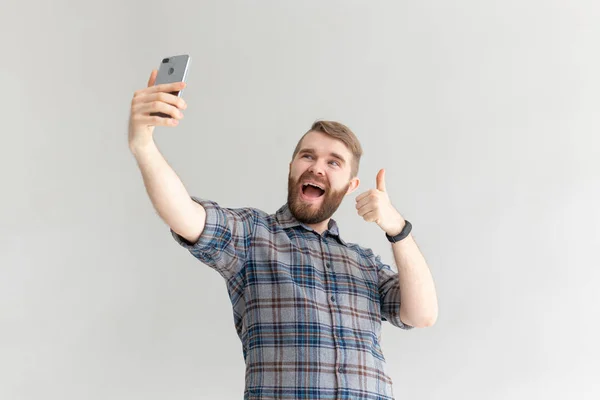 Olumlu bir komik yakışıklı hipster adam yan görünümü ve beyaz arka plan üzerinde bir akıllı telefon selfie alarak. Gadget'lar ve modern teknolojiler kavramı. — Stok fotoğraf