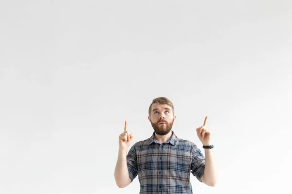 Überraschte junge Hipster-Mann mit Schnurrbart posiert auf weißem Hintergrund in Überraschung zeigt nach oben. Konzept der Überraschung und ein Ort für Werbung und Links — Stockfoto