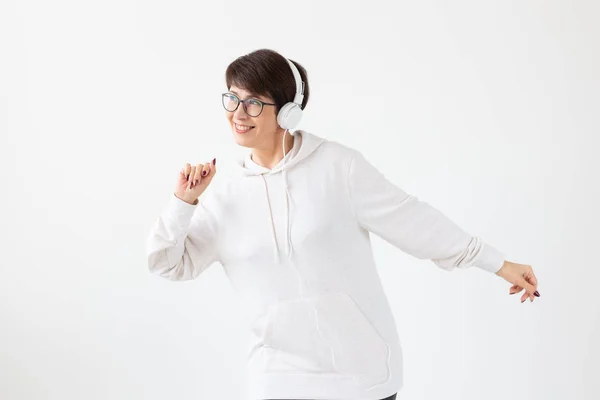 Całkiem chętnie w średnim wieku Kobieta w okularach i biały sweter słucha jej ulubionej muzyki ze słuchawkami na białym tle. Koncepcja subskrypcji radia i muzyki online. — Zdjęcie stockowe