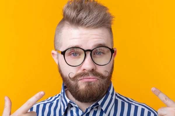 Encantador joven hombre hipster de moda con gafas y una barba se muestra posando sobre un fondo amarillo. Lugar para la publicidad. El concepto de confianza en sí mismo y éxito . — Foto de Stock