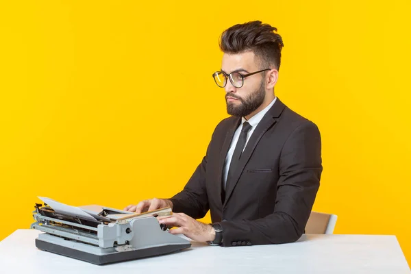 En ung, kjekk mann i formelle klær som skriver tekst på en skrivemaskin som poserer på gul bakgrunn. Reklameplass. Forretningskonsept . – stockfoto