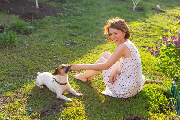 Mulher jovem bonito esbelto brinca com seu cão engraçado amado no quintal em um dia ensolarado de verão. Bonito conceito de animal de estimação . — Fotografia de Stock