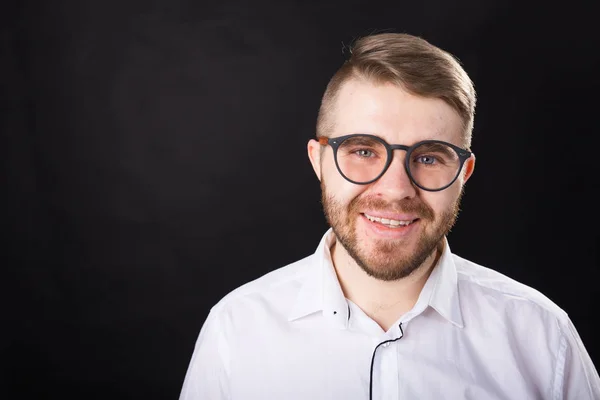 Retrato de joven hombre barbudo sonriente y en gafas sobre el fondo negro con espacio para copiar — Foto de Stock